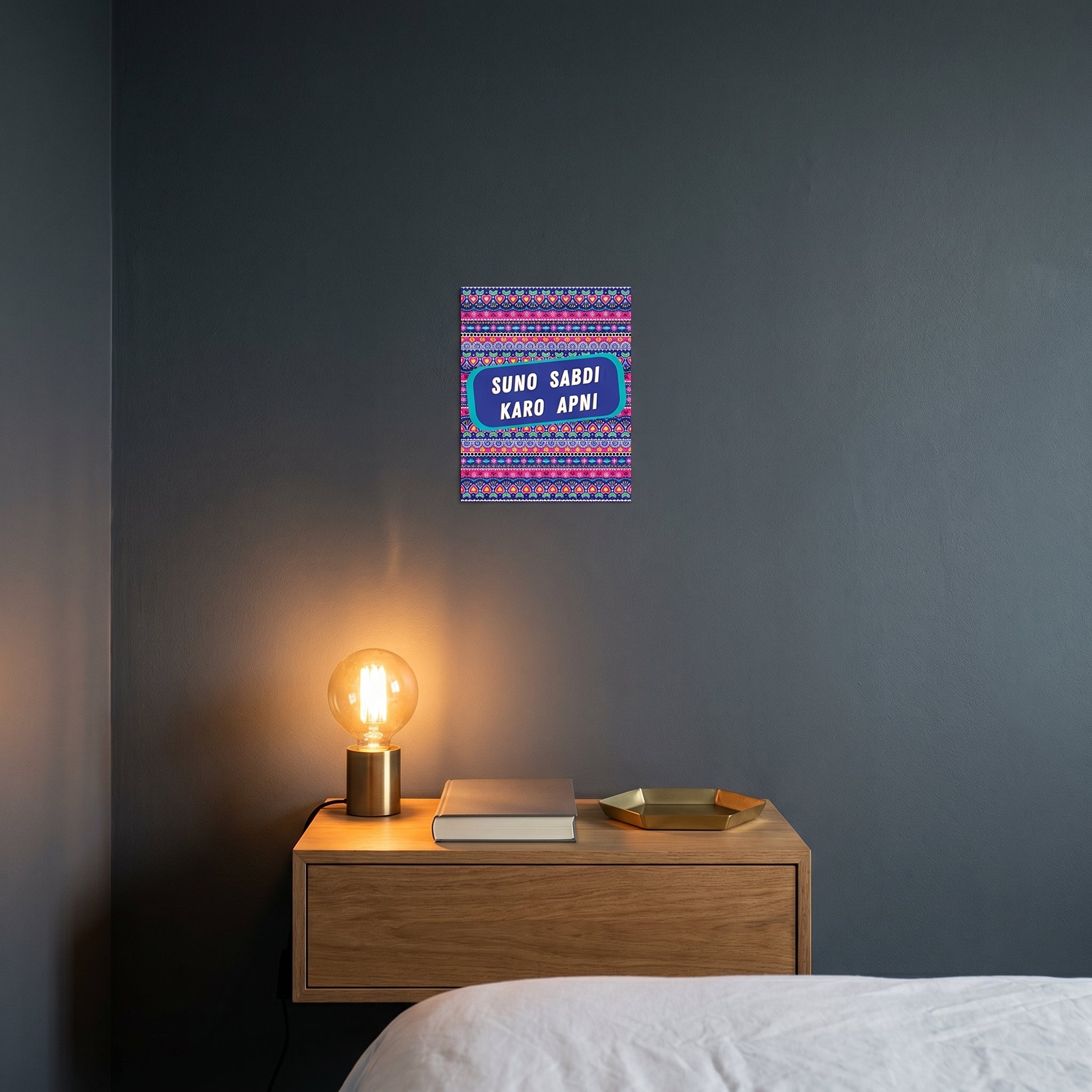 Contemporary bedroom nightstand featuring the Suno Sabdi Karo Apni framed poster catching warm ambient light from a lamp.
