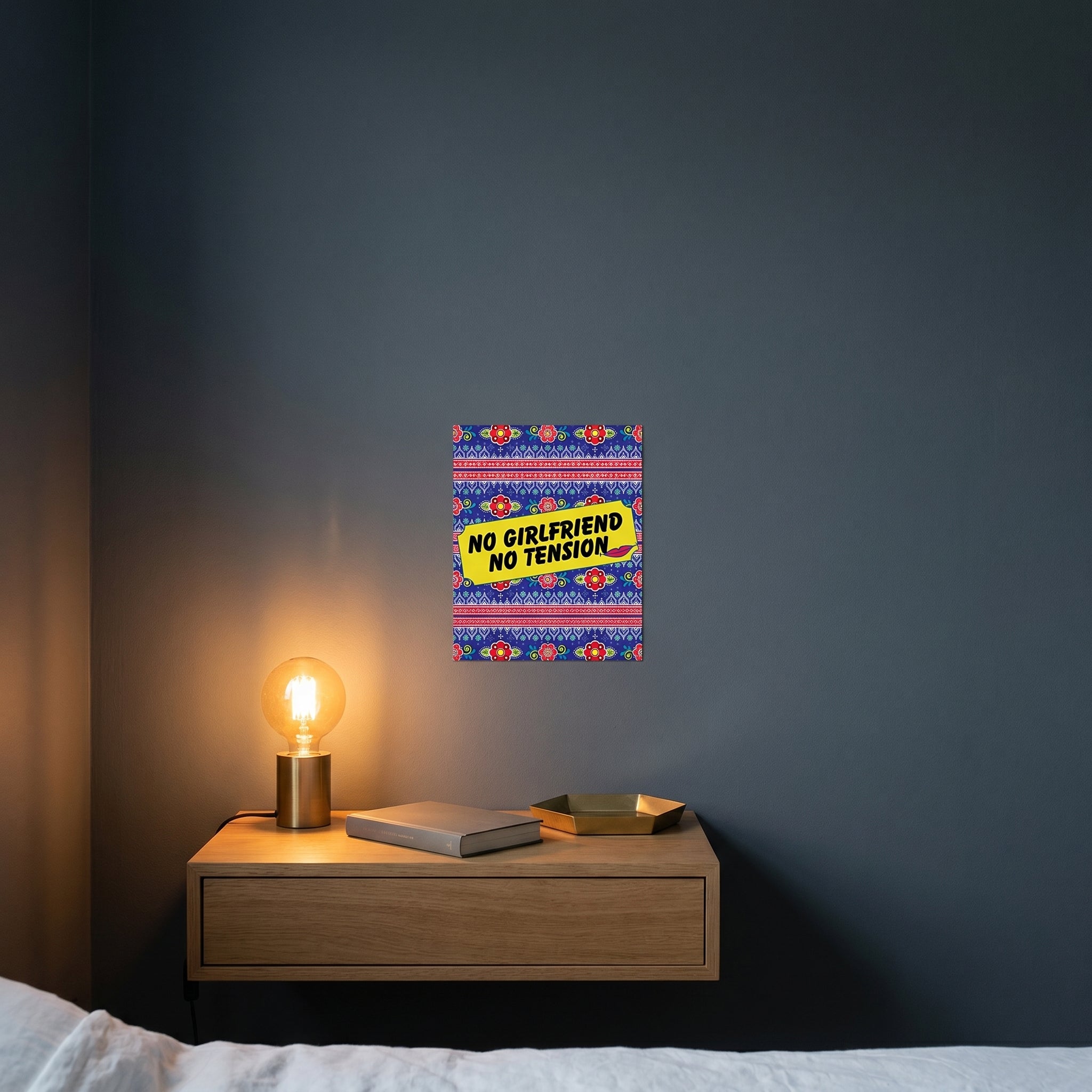 Pop-art style humorous Desi metal print catching warm ambient light from a lamp on a contemporary dark bedroom nightstand.
