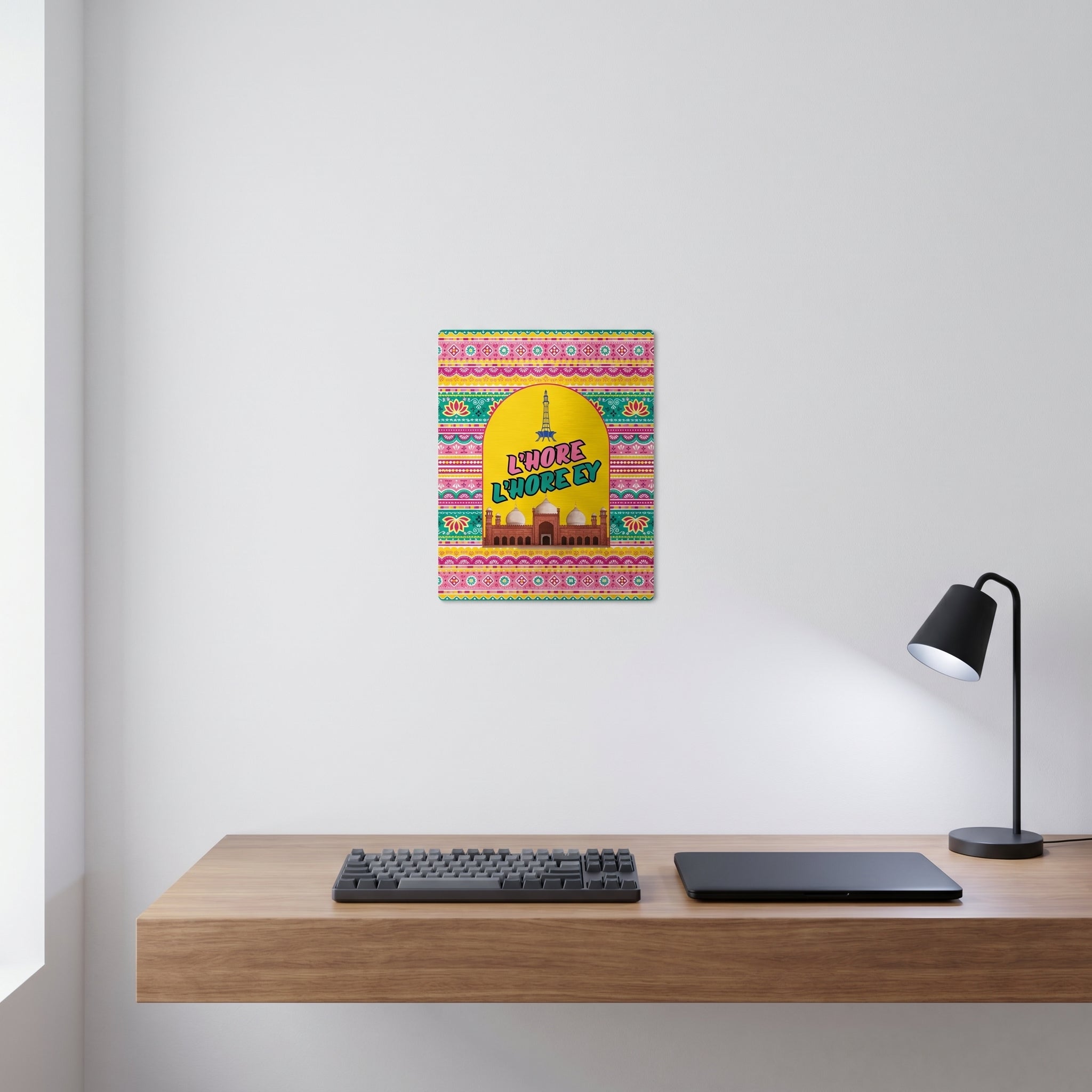 Traditional style Pakistani cultural slogan art print displayed on a crisp white wall behind a minimalist home office desk setup.
