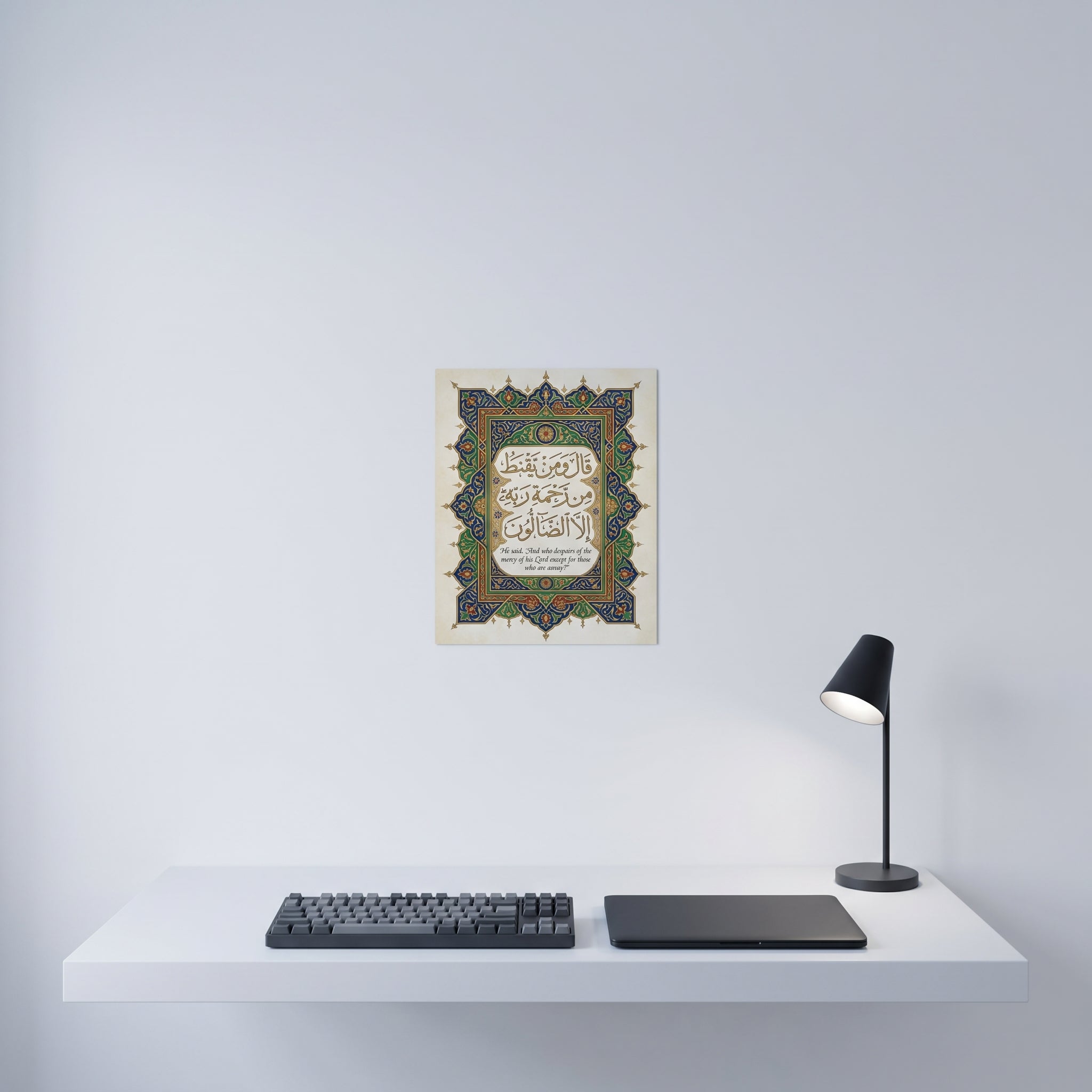 Traditional style Arabic calligraphy art print displayed on a crisp white wall behind a minimalist home office desk setup.